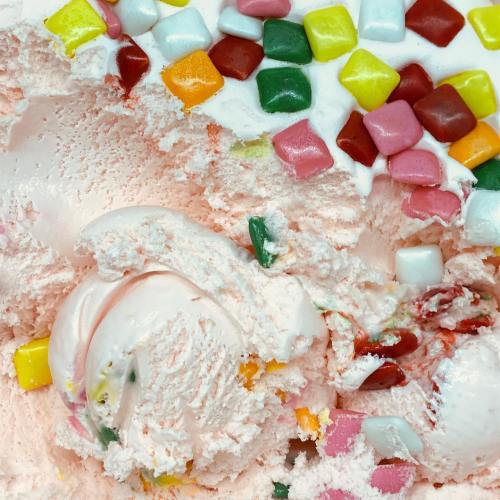 Close-up of pink ice cream with colorful candy pieces and a swirl of syrup on top.