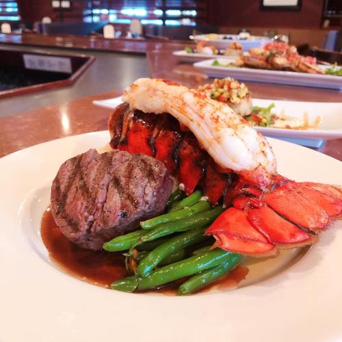 A gourmet plate featuring grilled lobster, filet mignon, green beans, and a rich sauce, elegantly presented.