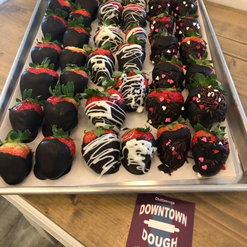 A tray of chocolate-covered strawberries, some decorated with white drizzle and colorful sprinkles, on a wooden table.