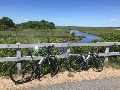 Two bicycles parked by a scenic river with lush greenery and a clear blue sky in the background.