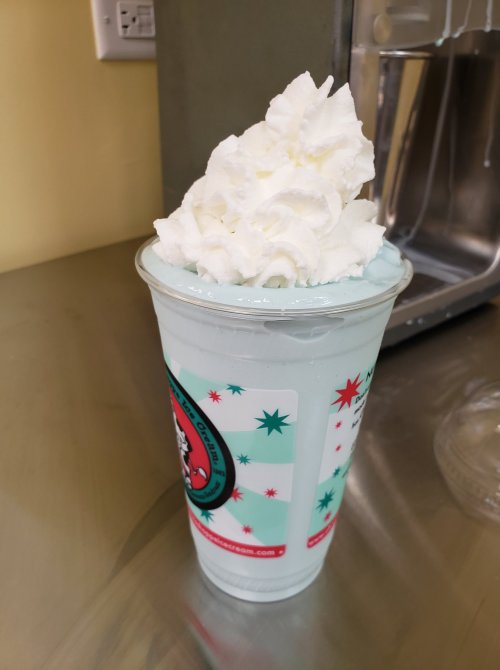 A tall cup filled with light blue mint-flavored ice cream topped with a generous swirl of whipped cream.