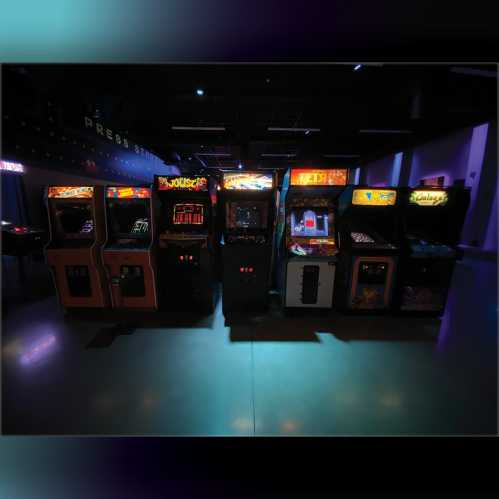 A row of vintage arcade game machines illuminated in a dimly lit room.