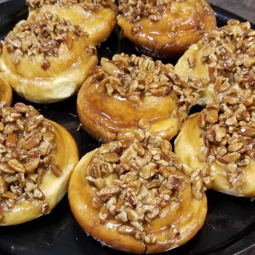 A close-up of sticky pecan rolls topped with caramelized pecans on a black platter.
