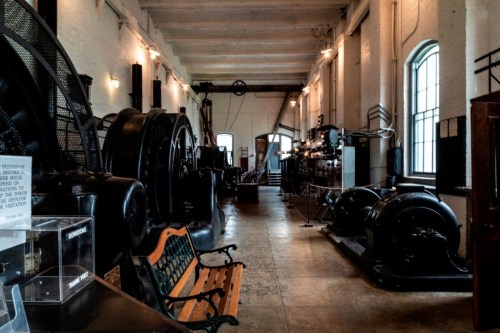 Interior of a historic industrial space featuring large machinery, a wooden bench, and soft lighting.