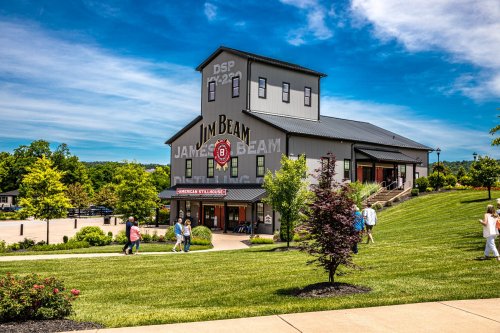 A sunny day at the Jim Beam distillery, featuring a large building and visitors walking on a green lawn.