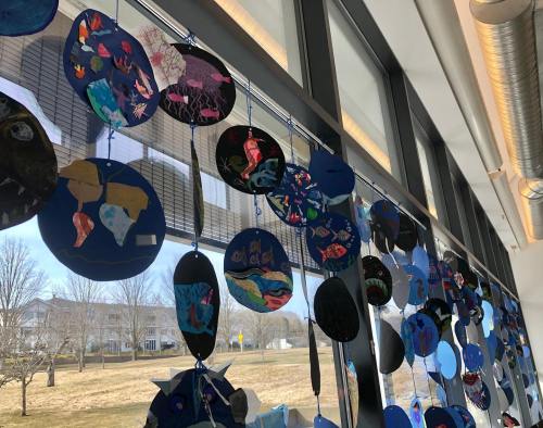 Colorful circular art pieces hanging from a window, showcasing various designs against a bright, sunny backdrop.