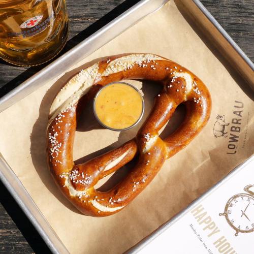 A large, soft pretzel with coarse salt, served with a small cup of mustard on a paper-lined tray.