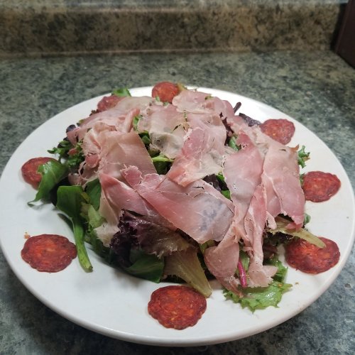 A plate of mixed greens topped with thinly sliced ham and garnished with circular slices of pepperoni.