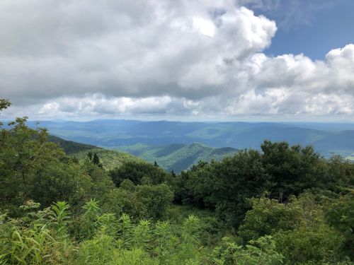 A panoramic view of lush green mountains under a partly cloudy sky, with valleys stretching into the distance.
