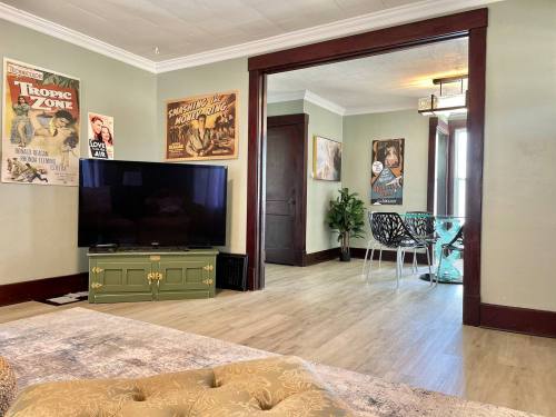 Cozy living room with a TV, vintage posters, and a glass dining area visible through an open doorway.