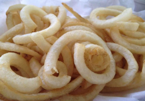 A close-up of golden, crispy curly fries piled in a white container.