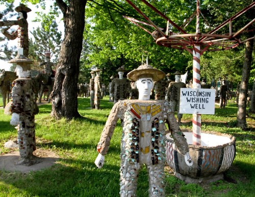 A whimsical garden featuring stone sculptures of people and a wishing well labeled "Wisconsin Wishing Well."