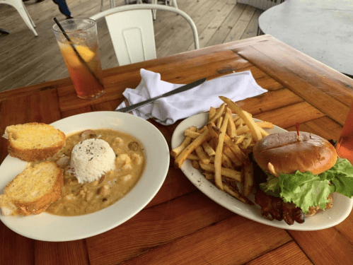 A plate with shrimp gumbo, rice, garlic bread, and a burger with lettuce, served with a side of fries and drinks.