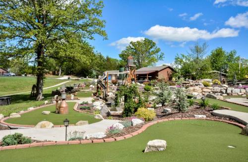 A scenic mini-golf course with lush greenery, rocks, and colorful flowers under a blue sky with fluffy clouds.