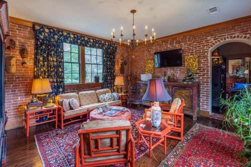 Cozy living room with brick walls, patterned curtains, vintage furniture, and warm lighting.