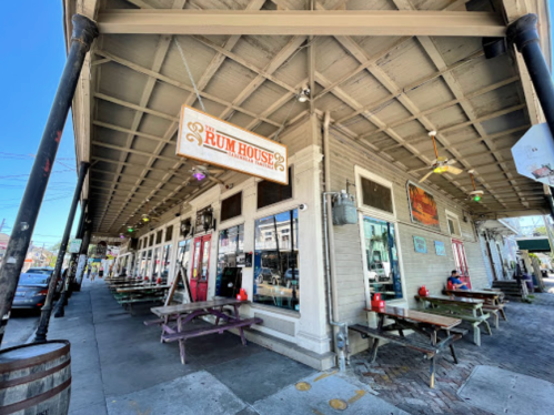 Exterior of The Rum House restaurant with outdoor seating, colorful signage, and a lively street scene.