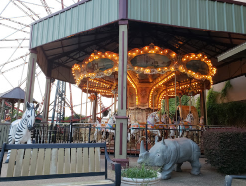 A carousel with illuminated horses and animal sculptures, including a zebra and a rhinoceros, in an amusement park setting.