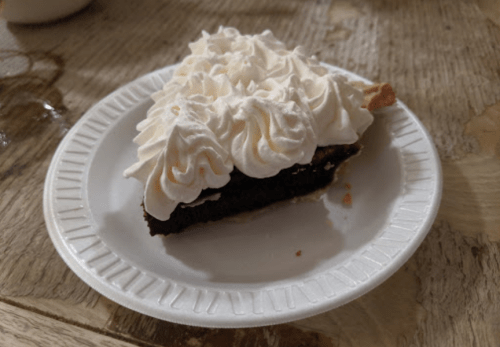 A slice of chocolate pie topped with whipped cream on a paper plate.