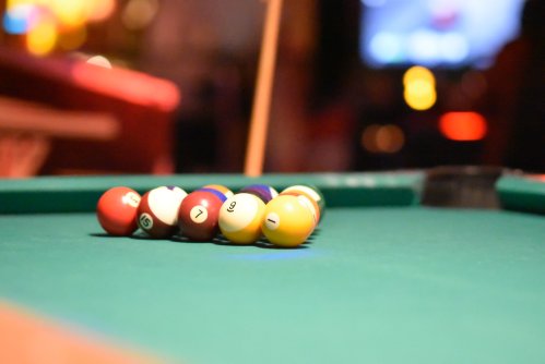 A close-up of a pool table with colorful billiard balls arranged in a triangle on a green felt surface.