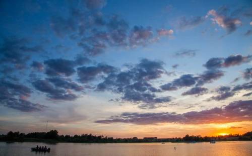 A serene sunset over a lake, with colorful clouds reflecting in the water and a small boat in the distance.
