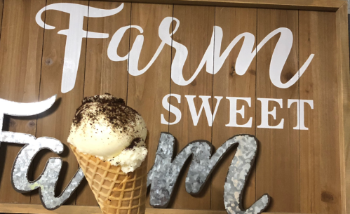 A close-up of an ice cream cone in front of a wooden sign that reads "Farm Sweet Farm."