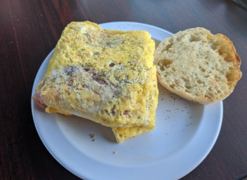 A plate with a folded omelet sprinkled with pepper and a piece of bread on the side.