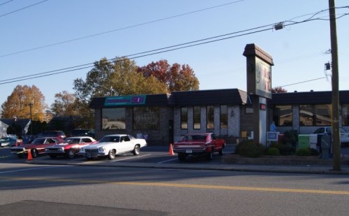 A diner with classic cars parked outside, surrounded by autumn trees and a clear blue sky.
