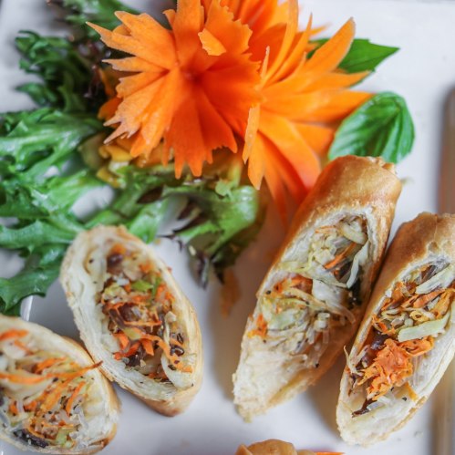 A plate of crispy spring rolls filled with vegetables, garnished with a carved carrot flower and fresh greens.
