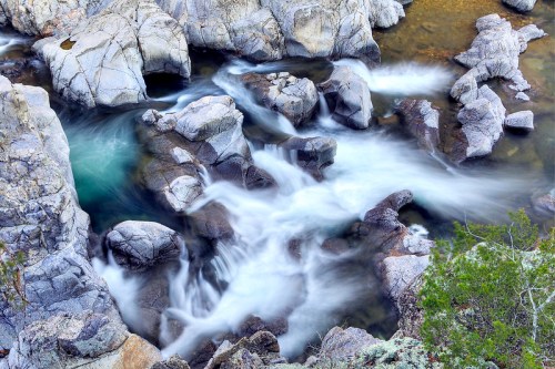 Aerial view of a rocky riverbed with flowing water and smooth stones, surrounded by greenery.