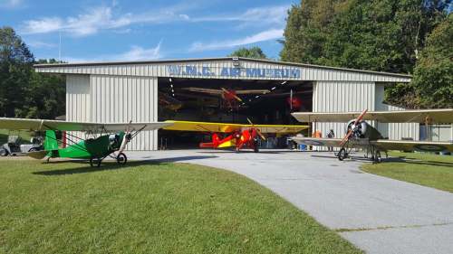 A hangar at the W.N. Clair Museum with vintage airplanes in front, surrounded by green grass and trees.