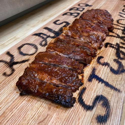 Sliced, glazed barbecue ribs arranged on a wooden cutting board with "KOALS BBQ" engraved.