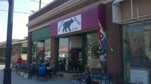 Exterior of Black Bear Café with outdoor seating, a "Open" sign, and a bear logo on the awning.