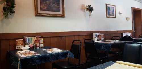 Cozy restaurant interior with wooden walls, black chairs, and tables set with menus and condiments.