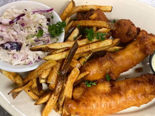 A plate of crispy fish fillets, golden fries, hush puppies, and a side of coleslaw garnished with parsley.