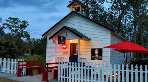 A charming white building with a bell tower, red umbrella, and picket fence, set in a lush green landscape.