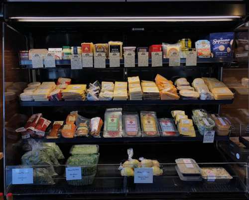 A display case filled with various cheeses, meats, and packaged food items on multiple shelves.