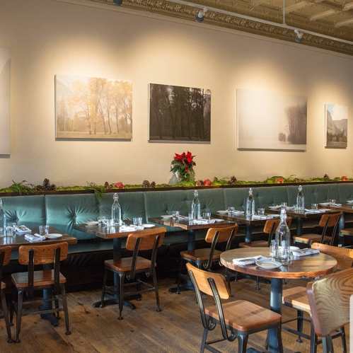 Cozy restaurant interior with green banquette seating, wooden tables, and art on the walls, decorated for the season.