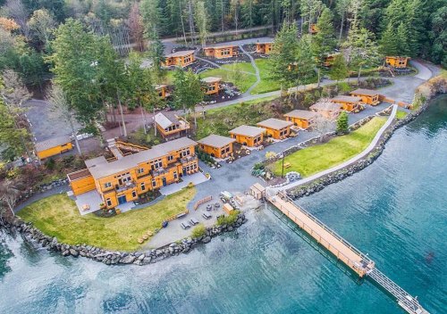 Aerial view of a waterfront lodge with multiple cabins surrounded by trees and a dock extending into the water.