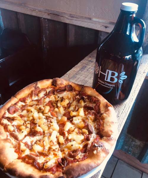 A delicious pizza topped with sausage and pineapple, next to a brown growler labeled "HB Sisters Oregon."