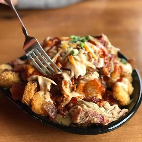 A plate of loaded tater tots topped with barbecue sauce, cheese, and green onions, with a fork digging in.