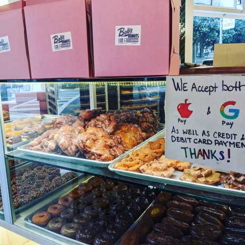 A display case filled with various donuts and pastries, with a sign indicating payment options accepted.