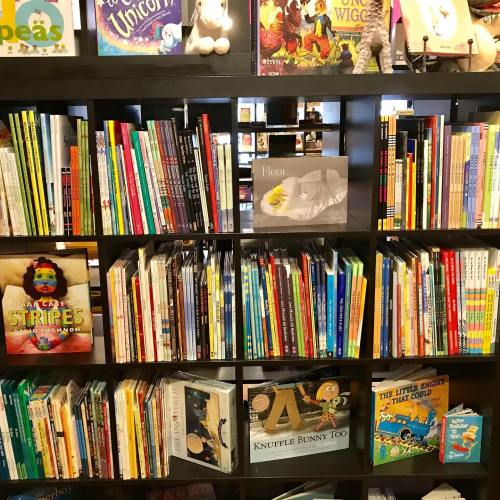 A colorful bookshelf filled with various children's books and plush toys on top.