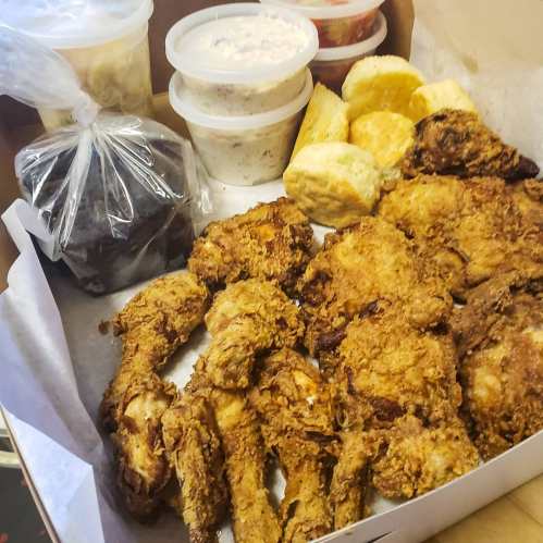 A takeout box filled with fried chicken, biscuits, and containers of sides like coleslaw and dessert.