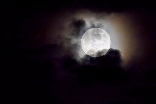 A bright full moon partially obscured by dark, swirling clouds in a night sky.
