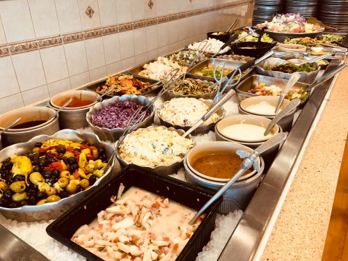 A buffet spread featuring various salads, vegetables, and dressings arranged in bowls on a table.
