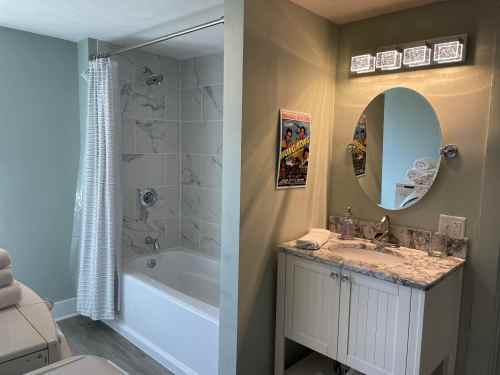 A modern bathroom featuring a shower-tub combo, a marble vanity, and a vintage poster on the wall.