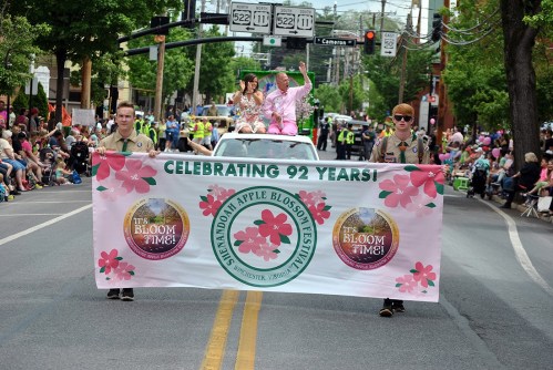 A parade scene with two individuals holding a banner celebrating 92 years of the Shenandoah Apple Blossom Festival.