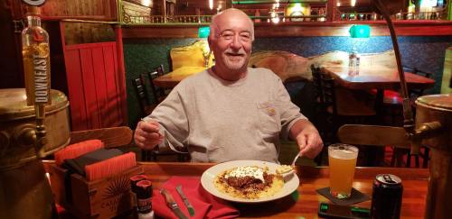 A smiling man sits at a restaurant table with a plate of food and drinks, enjoying his meal in a cozy setting.