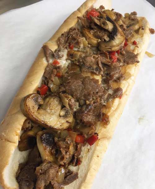 A loaded sandwich with sliced beef, sautéed mushrooms, onions, and red peppers on a toasted hoagie roll.
