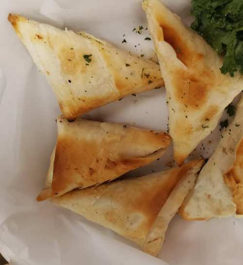 A plate of golden-brown triangular pastries, garnished with parsley, on a white background.